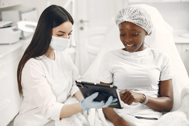 A skincare consultant and client review information on a tablet in a bright consultation room.