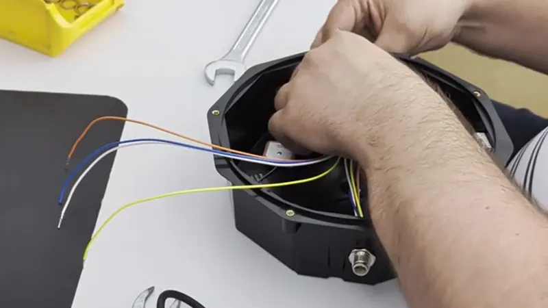 Hands assemble colored wiring inside an electronic device housing on a workbench.